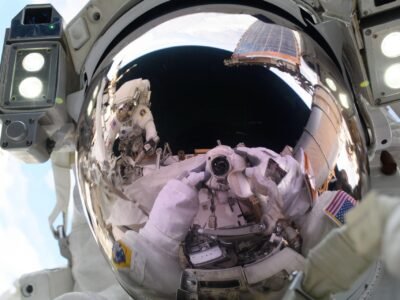 A astronauta da NASA e engenheira de voo da Expedição 72, Anne McClain, aponta uma câmara na sua direção e tira um “selfie espacial” durante uma caminhada espacial para atualizar o sistema de geração de energia da estação orbital e realocar uma antena de comunicação. Refletida no visor do seu capacete está a sua colega de caminhada espacial e astronauta da NASA, Nichole Ayers.